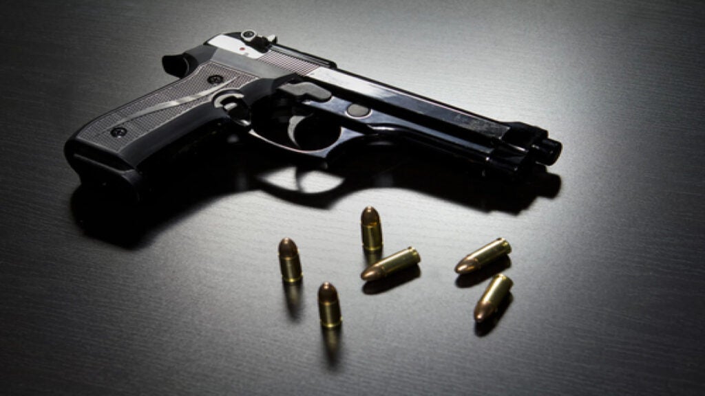 Gun on a table with bullets scattered around it.|