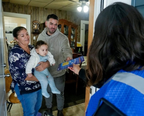 man, woman, baby at front door speaking with election worker