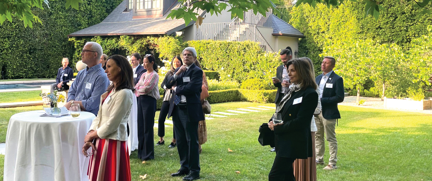 people in business attire stand outside a home while a speaker is talking