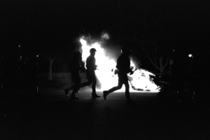three figures silhouetted against a fire burning in the background