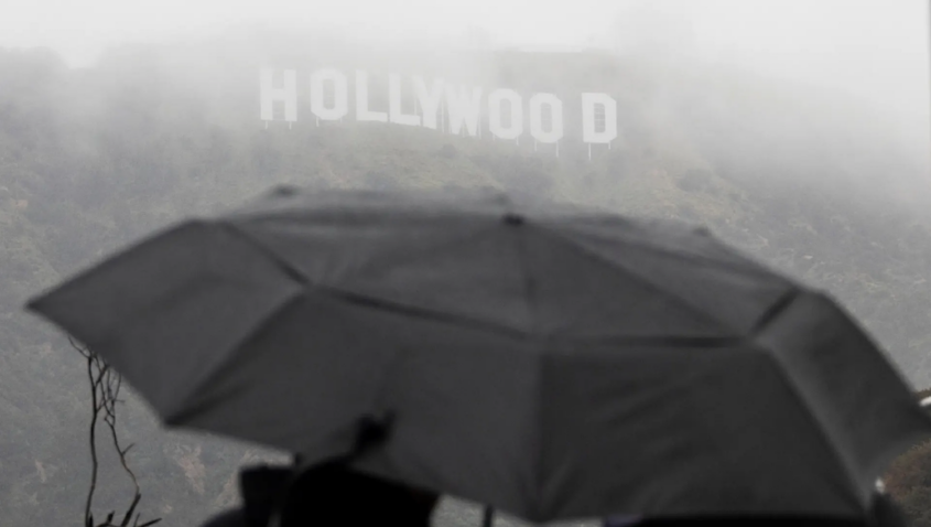 People with umbrella at Hollywood sign during storm