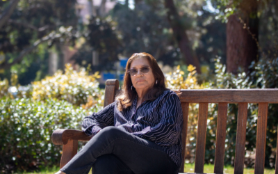 woman in blue top and jeans is surrounded by foliage as she sits on a bench