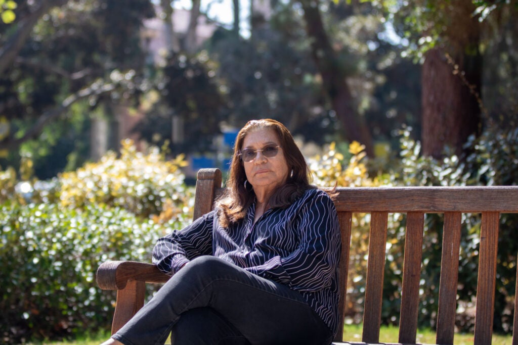 woman in blue top and jeans is surrounded by foliage as she sits on a bench