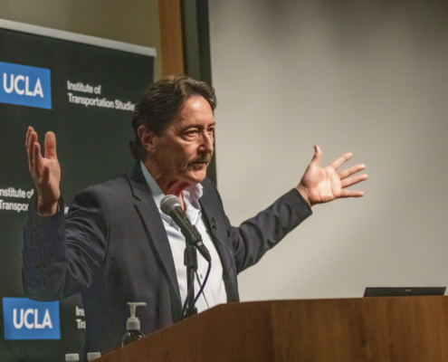 man at podium gestures with arms spread wide