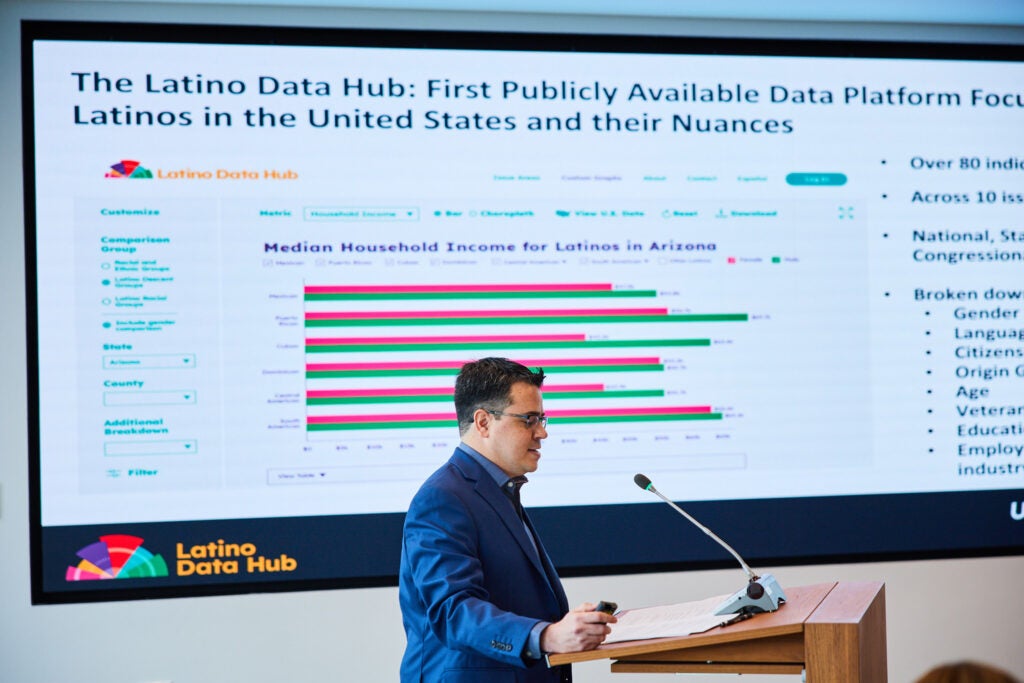 man in blue suit talks at podium with a chart on screen behind him