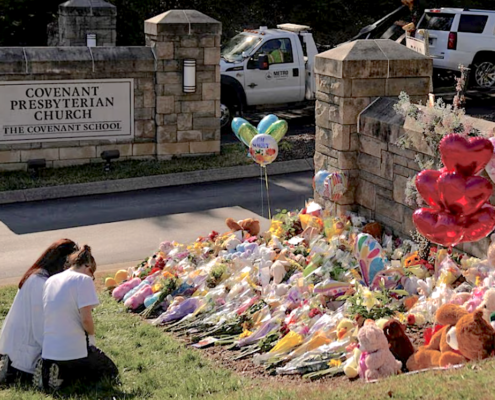 two people kneeling in front of flowers at a makeshift memorial