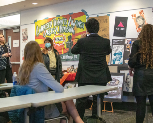 people stand in front of a wall covered with posters, photos and artifacts relating to homelessness
