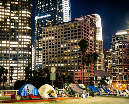 tents line a city street at night beneath skyscrapers in downtown Los Angeles