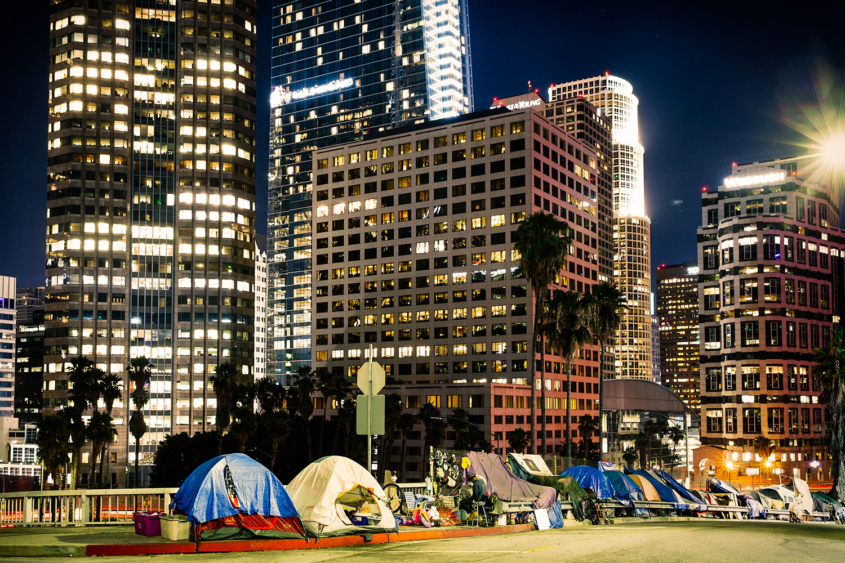 tents line a city street at night beneath skyscrapers in downtown Los Angeles