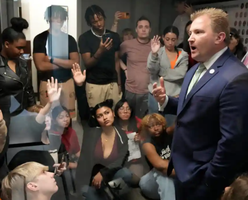 Man in suit speaks to room filled with young people