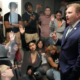 Man in suit speaks to room filled with young people