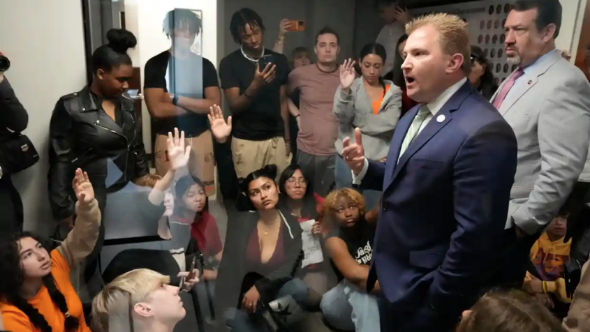 Man in suit speaks to room filled with young people