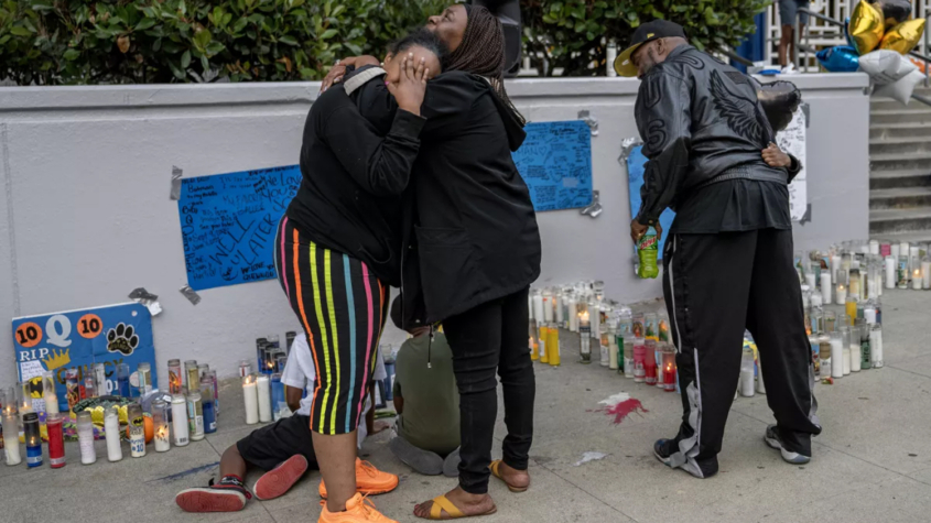 people mourn near sidewalk memorial for slain youth