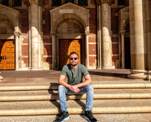 young person in jeans and sunglasses sits on steps of university building