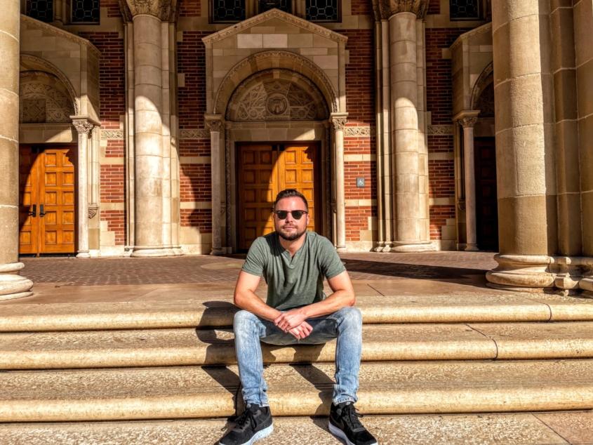 young person in jeans and sunglasses sits on steps of university building