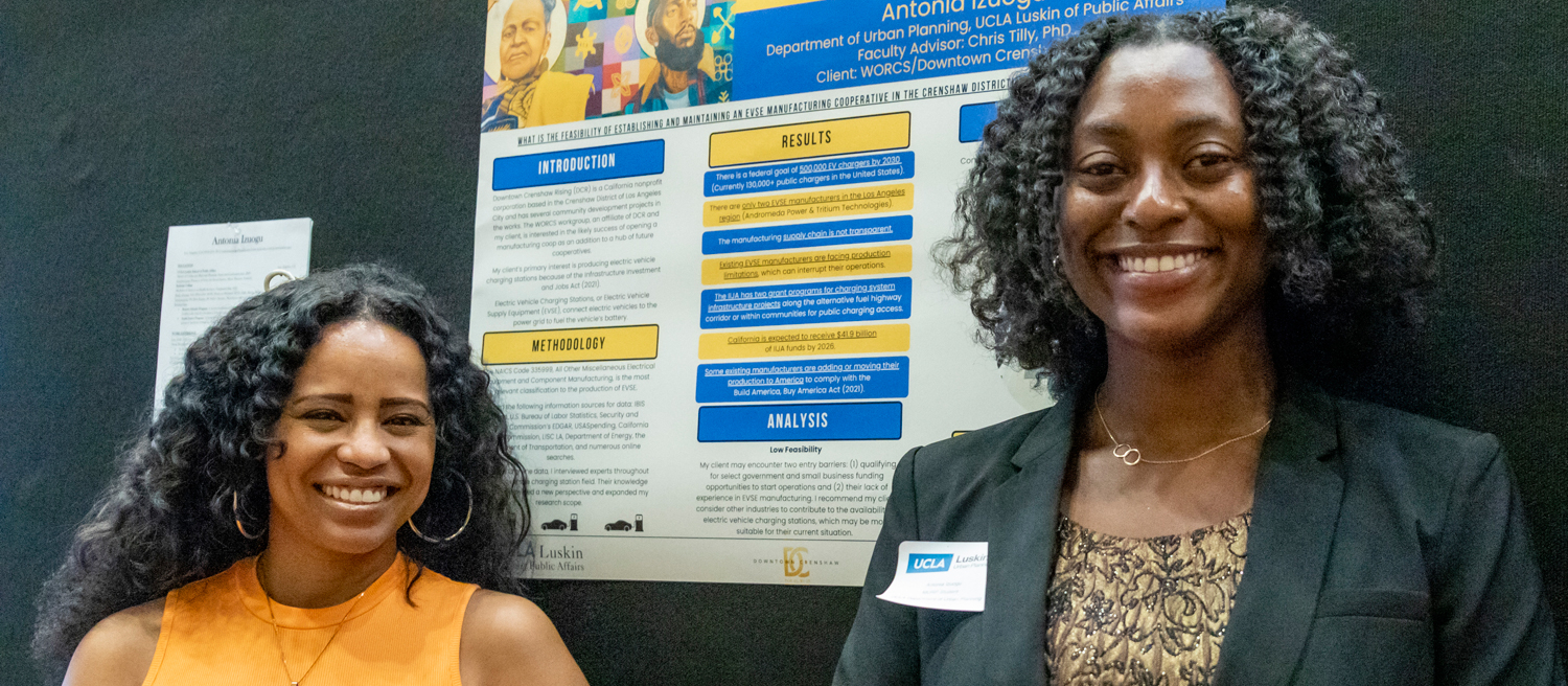 two Black women pose in front of a poster about a research project