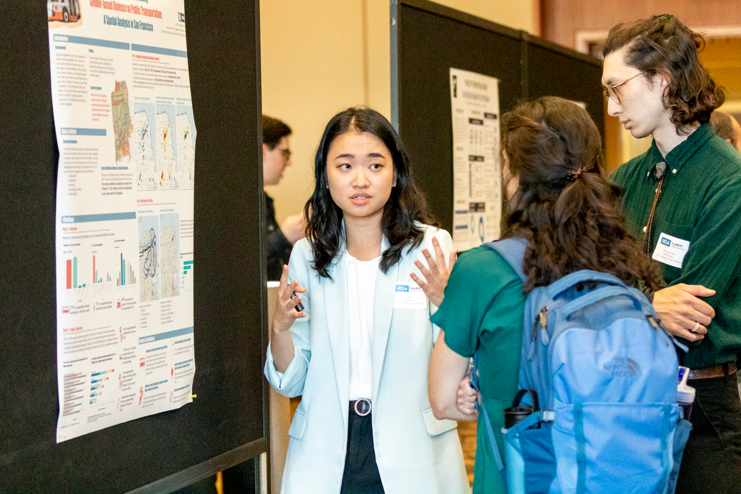 young woman in blue jacket gestures while talking about research shown on poster to her right