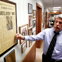 man in corridor pointing to newspaper front page