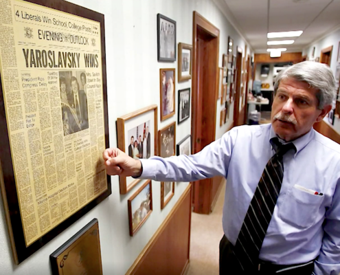 man in corridor pointing to newspaper front page