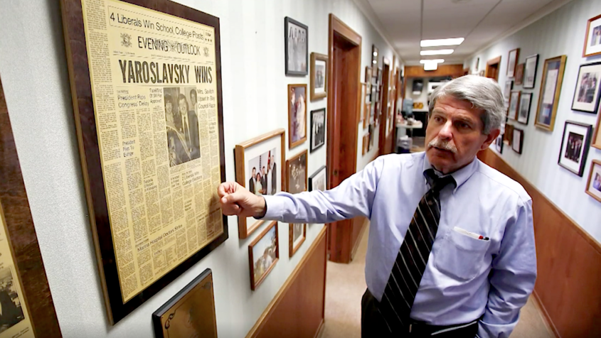 man in corridor pointing to newspaper front page