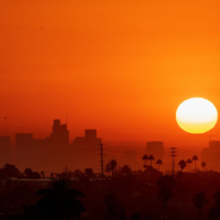 sun hangs low over city with sky looking orange Photo by johnemac72/iStock