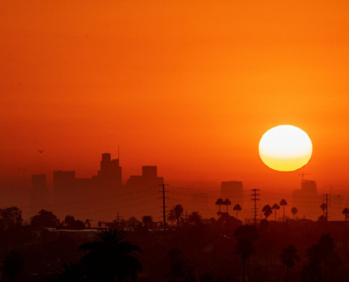 sun hangs low over city with sky looking orange Photo by johnemac72/iStock