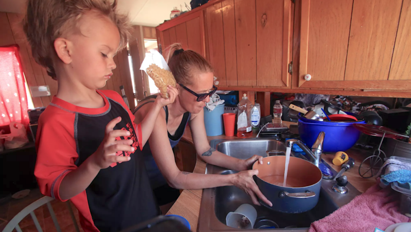 Woman fills pot with water from sink as child holds macaroni