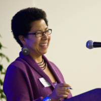 woman wearing purple top smiles while talking at a podium