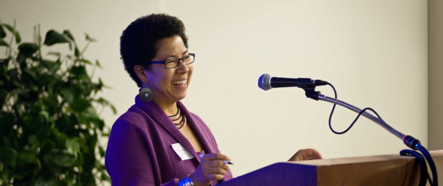 woman wearing purple top smiles while talking at a podium