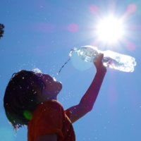 Child outdoors pouring water on self.
