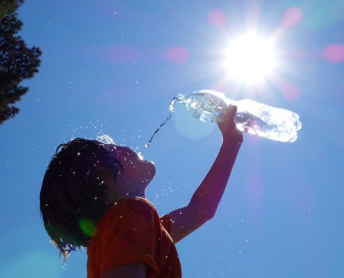 Child outdoors pouring water on self.