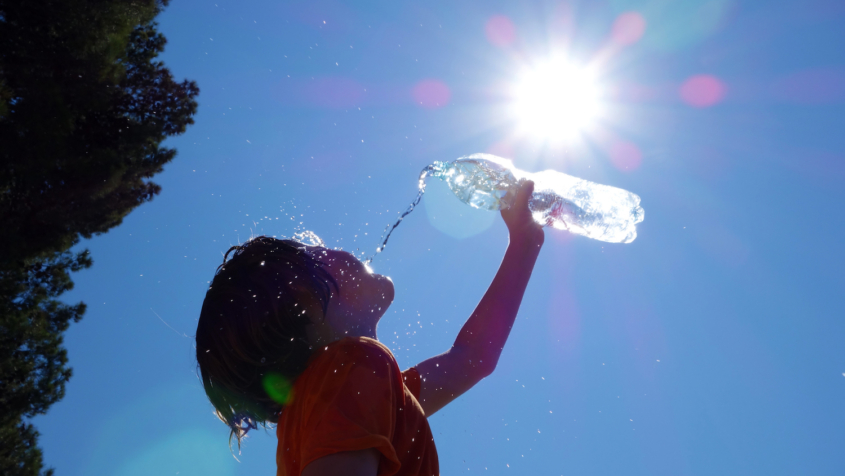 Child outdoors pouring water on self.