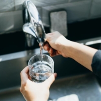 hands turn faucet to run water into a glass