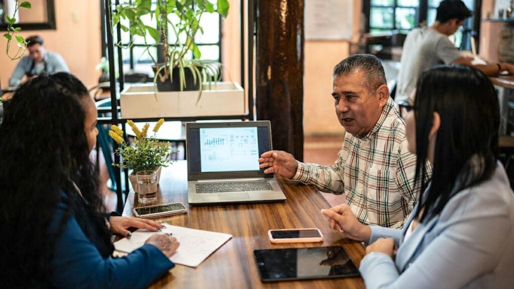 Three people at table in coffee shop with laptop open