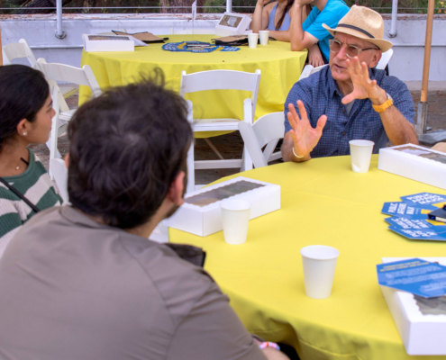 Man in glass and hand sits at table with two students