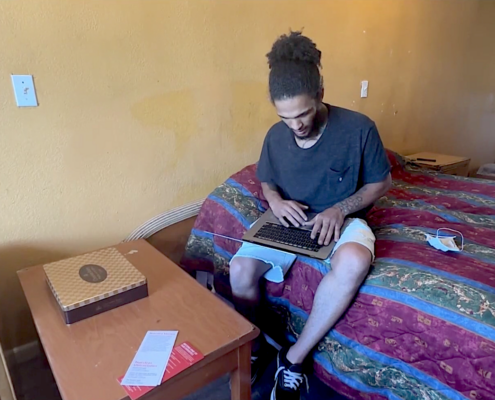 Man on bed in hotel room, typing on laptop