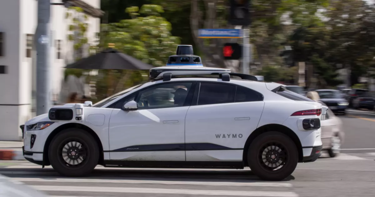 a white driverless vehicle is shown from the left side sitting on a city street
