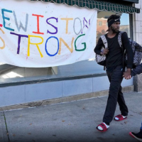 two people holding hands in front of "Lewiston Strong" banner