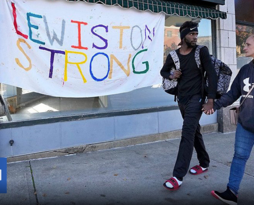 two people holding hands in front of "Lewiston Strong" banner