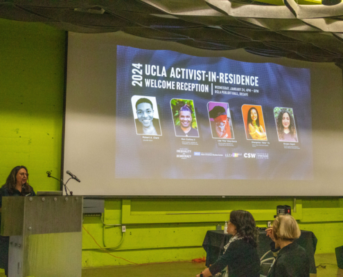 woman at podium with image projected on large screen behind her that shows activists' pictures and names