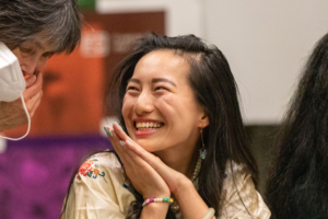 young Asian woman smiles broadly while speaking with someone to her right