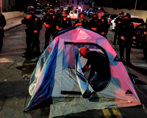 Man setting up tent in street in front of police officers