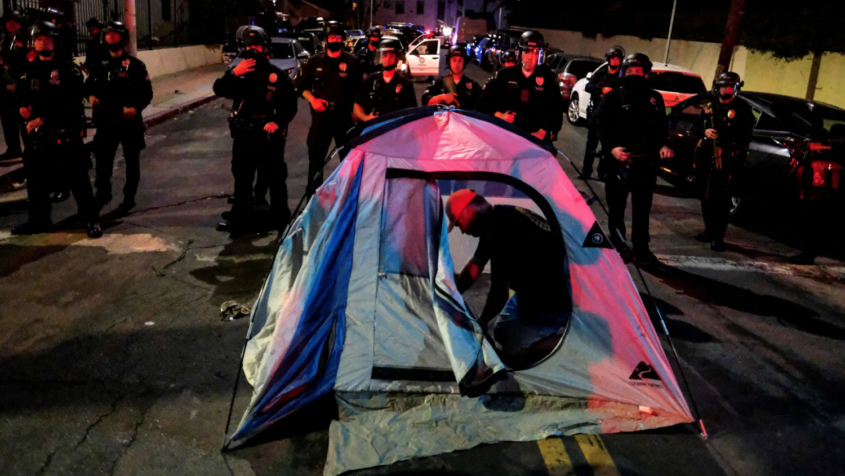 Man setting up tent in street in front of police officers