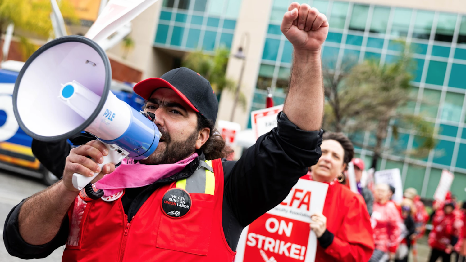 Picket line with man in red vest with megaphone in front