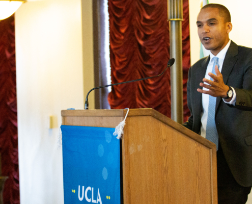 man in suit and tie gestures with one hand from podium
