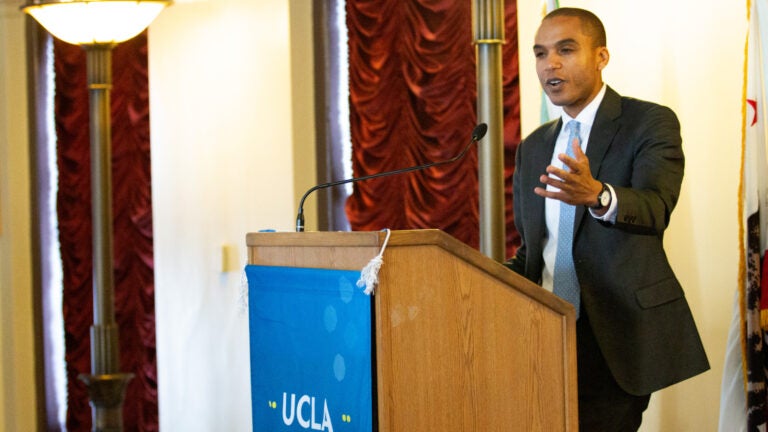 man in suit and tie gestures with one hand from podium