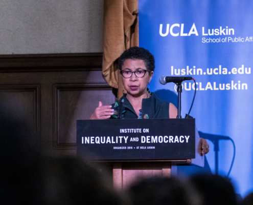 Black woman wearing glasses speaks from a podium with a UCLA Luskin backdrop behind her