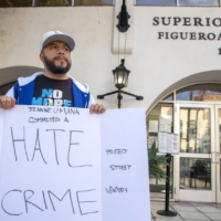 Man in hat holding sign that says "Hate Crime"