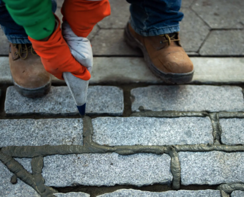 hands in red work gloves squirting grout into sidewalk cracks
