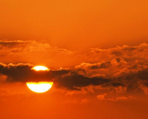 sun partially covered by clouds against orange sky